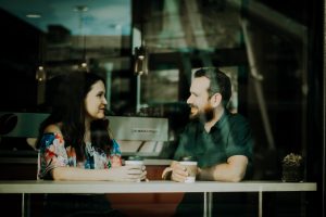 Man and woman having coffee at a coffee shop in the front window smiling and talking
