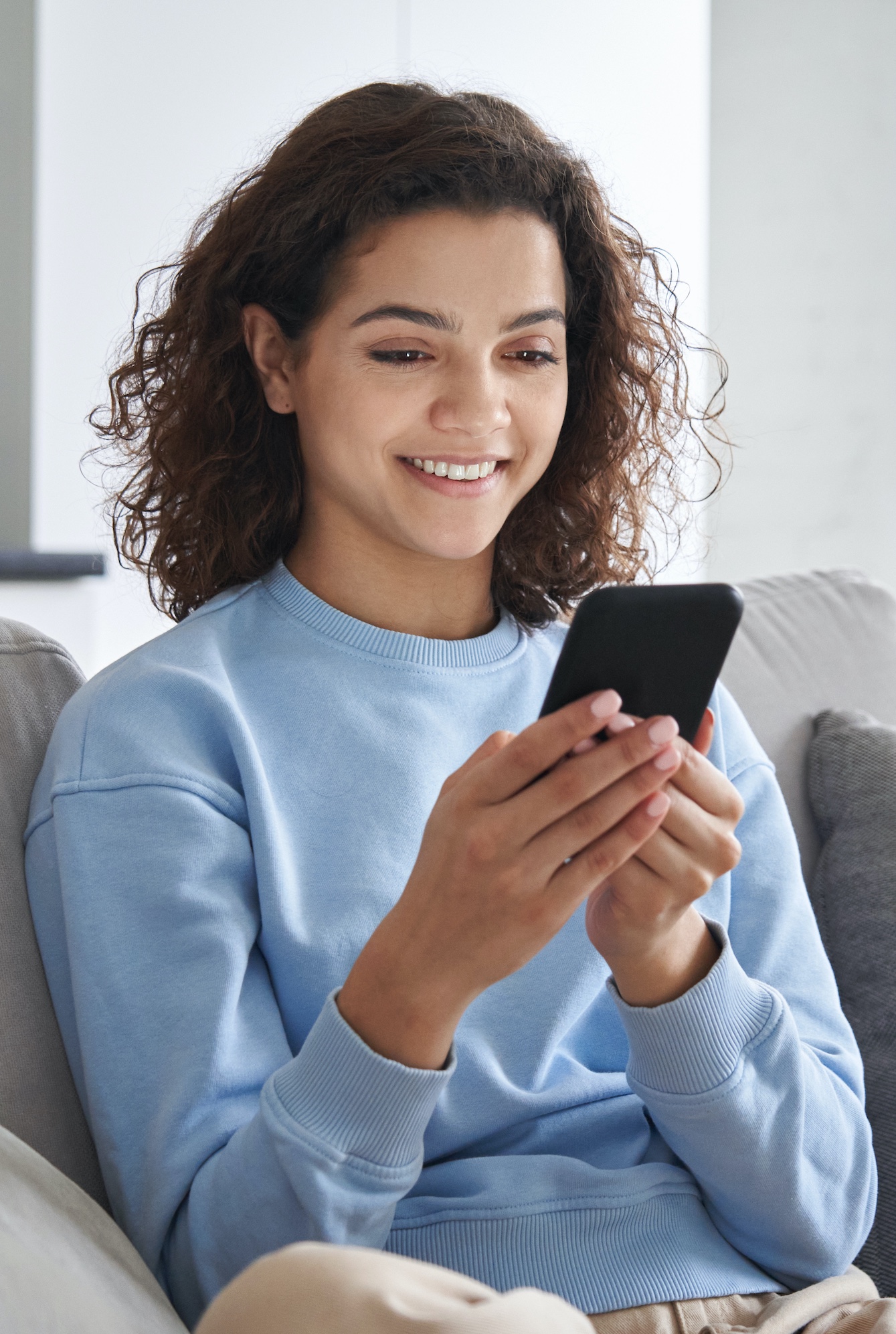 Woman on couch smiling looking at smart phone