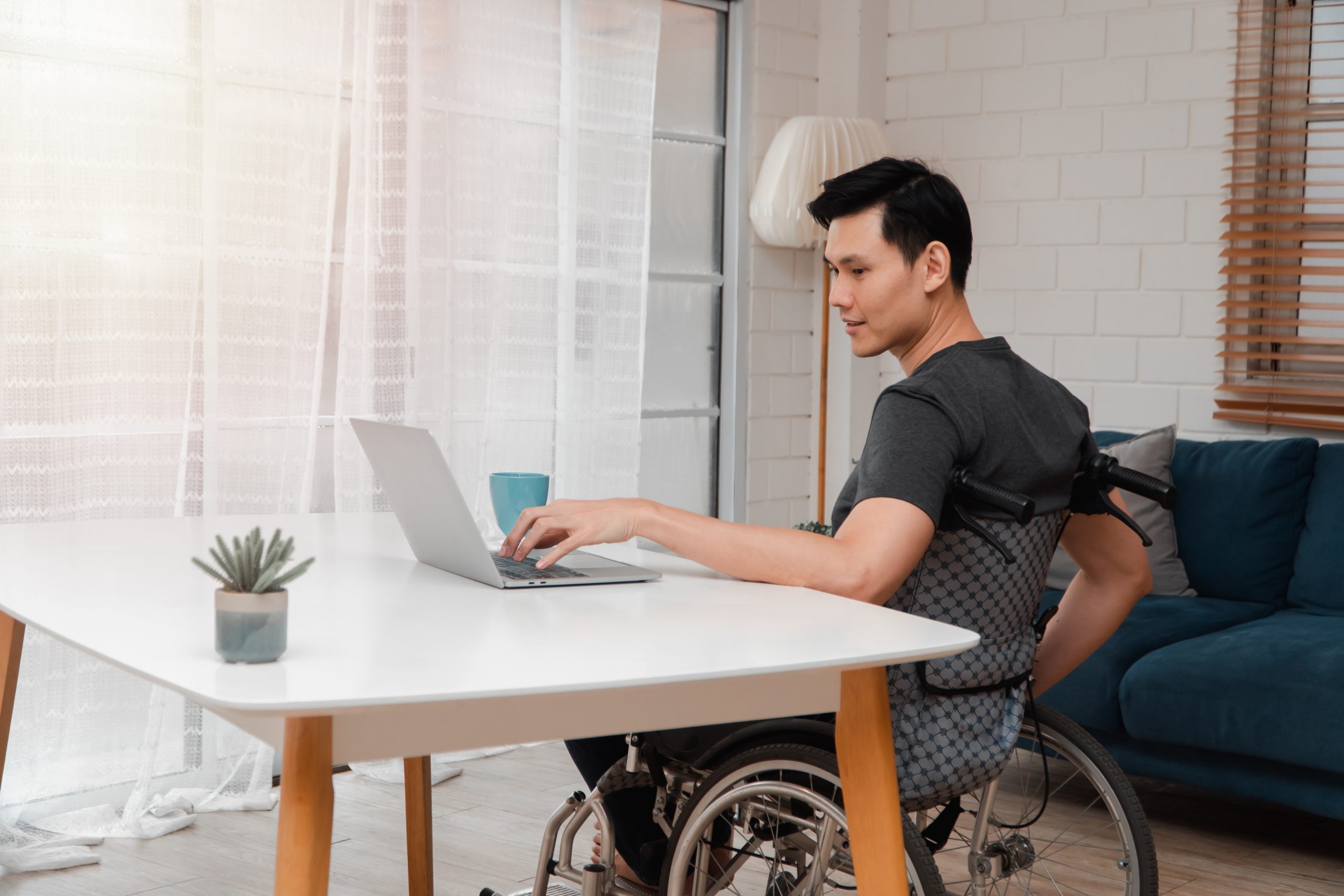 Happy disabled Asian man sitting in a wheelchair and looking at computer